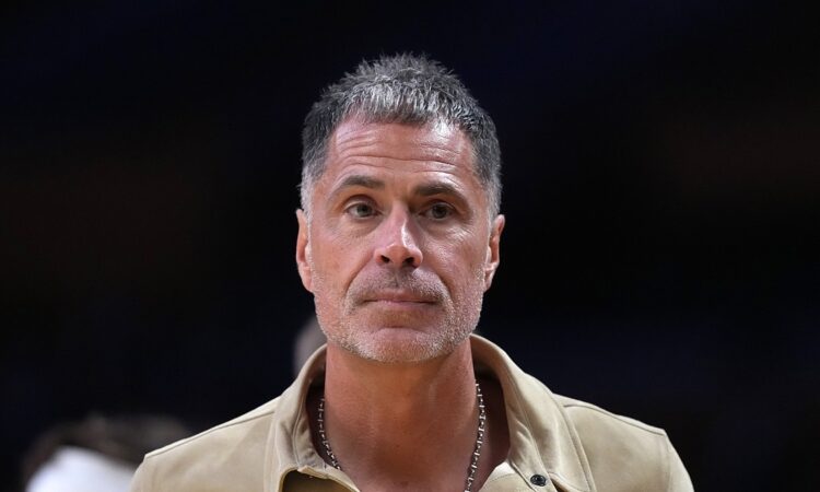 Los Angeles Lakers general manager Rob Pelinka, wearing a tan suede shirt jacket, looks on from courtside.