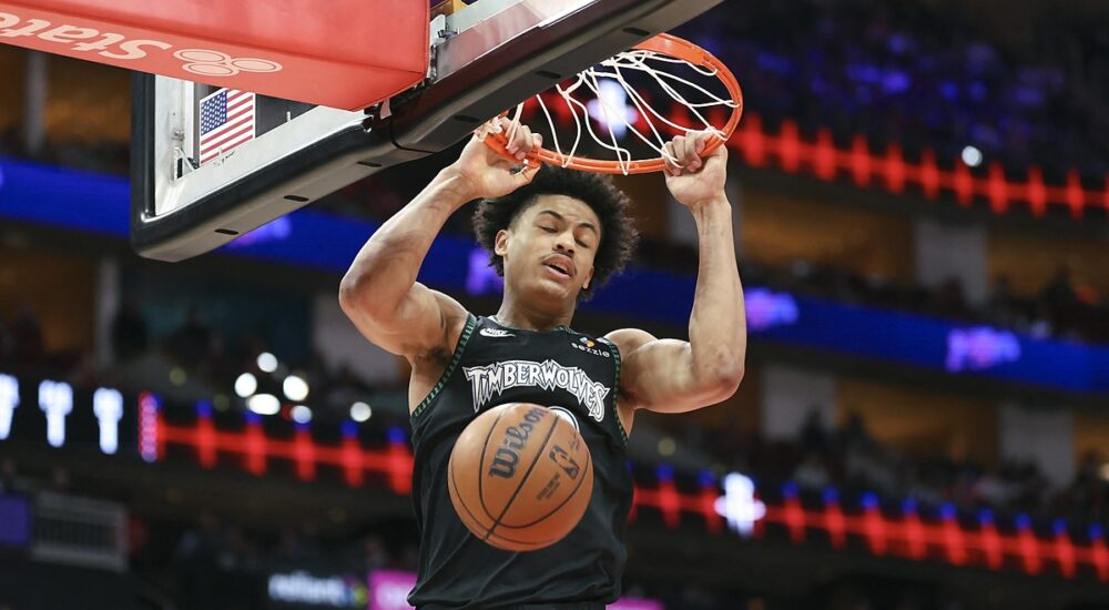 Minnesota Timberwolves forward Joan Beringer hangs on the rim with both hands as the ball drops through the net.