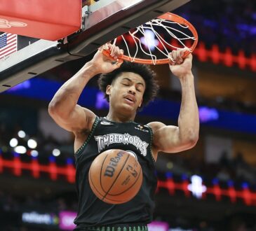 Minnesota Timberwolves forward Joan Beringer hangs on the rim with both hands as the ball drops through the net.