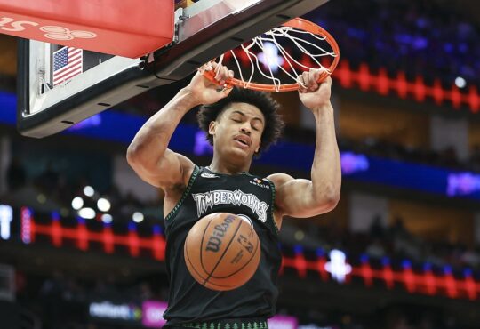 Minnesota Timberwolves forward Joan Beringer hangs on the rim with both hands as the ball drops through the net.