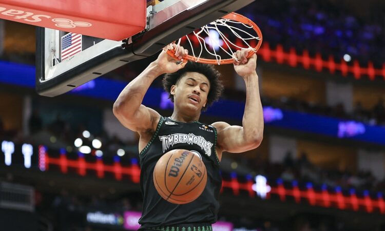 Minnesota Timberwolves forward Joan Beringer hangs on the rim with both hands as the ball drops through the net.