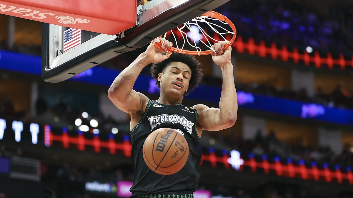 Minnesota Timberwolves forward Joan Beringer hangs on the rim with both hands as the ball drops through the net.