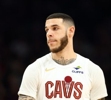 Cleveland Cavaliers guard Lonzo Ball looks toward the court in a white Cavs jersey.