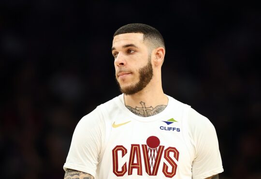 Cleveland Cavaliers guard Lonzo Ball looks toward the court in a white Cavs jersey.