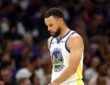Golden State Warriors guard Stephen Curry looks down as he walks across the court in a white Warriors jersey.