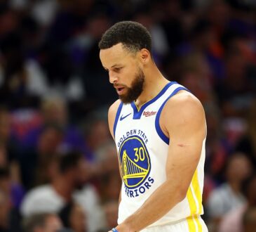 Golden State Warriors guard Stephen Curry looks down as he walks across the court in a white Warriors jersey.