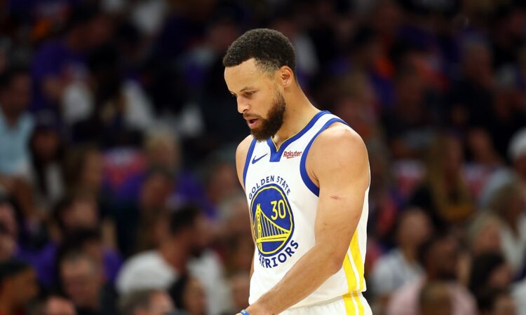Golden State Warriors guard Stephen Curry looks down as he walks across the court in a white Warriors jersey.