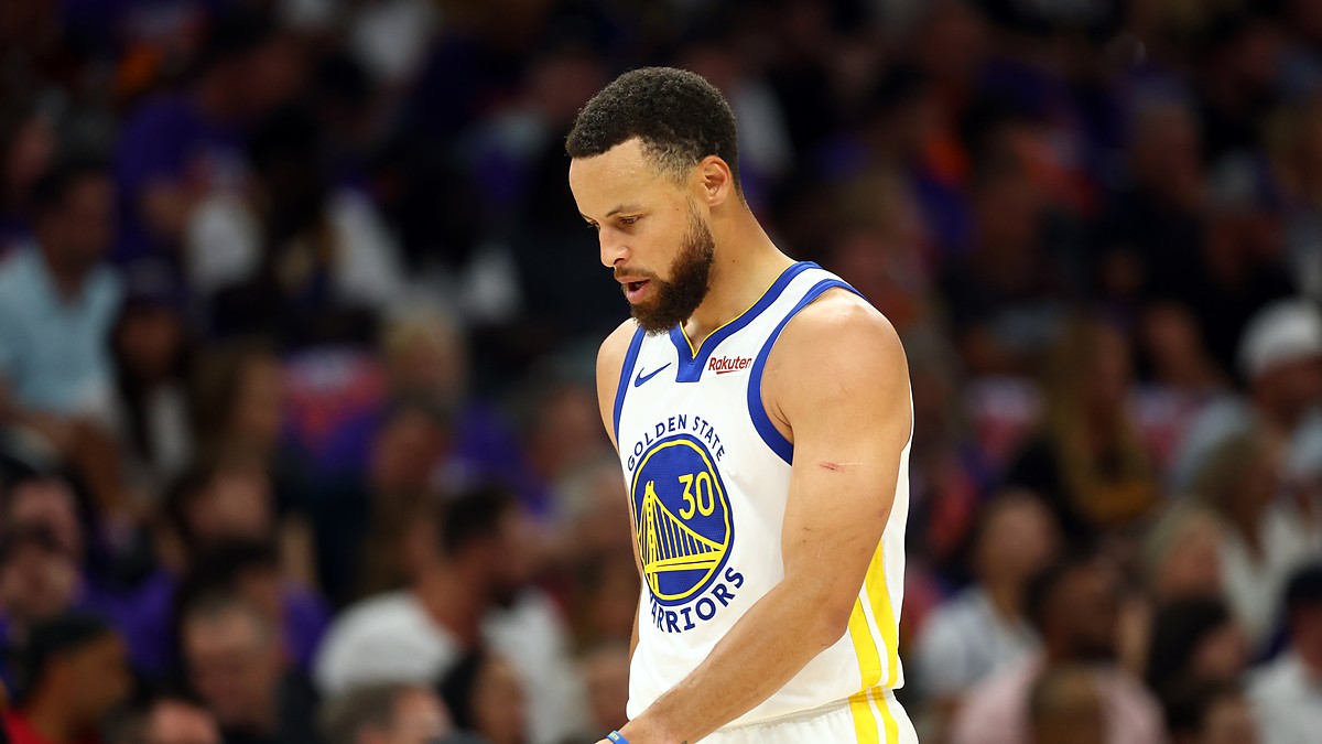 Golden State Warriors guard Stephen Curry looks down as he walks across the court in a white Warriors jersey.