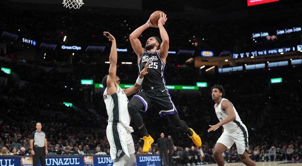 Sacramento Kings guard Ben Simmons rises for a shot between two San Antonio Spurs defenders near the basket.