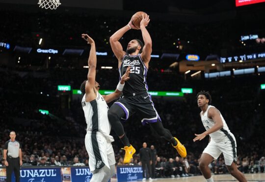 Sacramento Kings guard Ben Simmons rises for a shot between two San Antonio Spurs defenders near the basket.