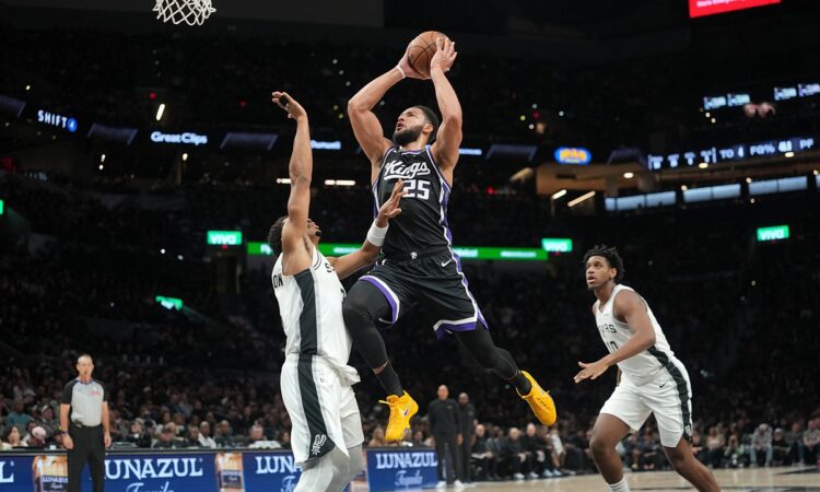 Sacramento Kings guard Ben Simmons rises for a shot between two San Antonio Spurs defenders near the basket.